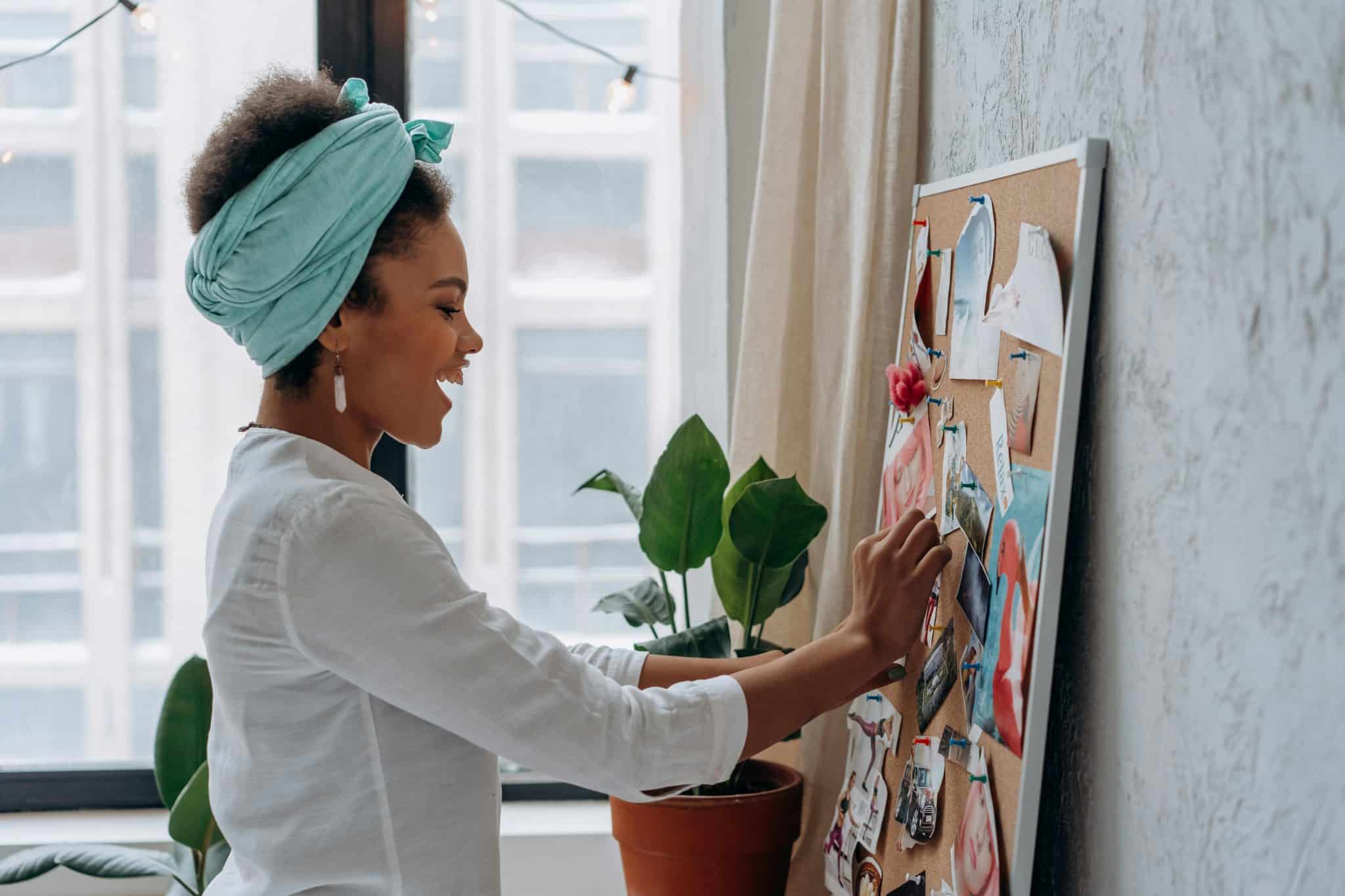 miling woman adding a sticky note to her vision board during a goal-setting session.